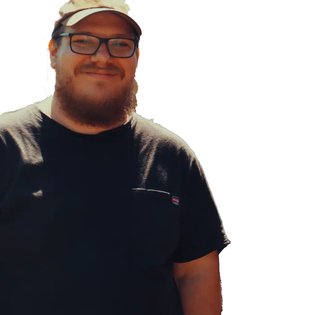 Smiling person wearing glasses and a cap, dressed in a black T-shirt, with a transparent background.